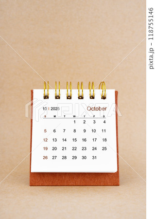 October 2025 white desk calendar on brown background. 118755146