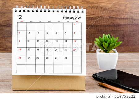 February 2025 desk calendar on wooden table with black smartphone. February 2025 desk calendar on wooden table with black smartphone. 118755222
