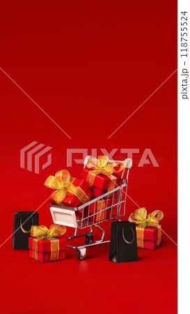 Supermarket trolley with red box with gold bows and black shopping bags. The concept of buying gifts for holidays and sales. Discounts, Black Friday. Red background, Copy space vertical banner Supermarket trolley with red box with gold bows and black shopping bags. The concept of buying gifts for holidays and sales. Discounts, Black Friday. Red background, Copy space vertical banner 118755524