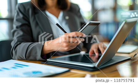 Professional Woman Multitasking With a Smartphone and Laptop in a Modern Office Setting 118755791