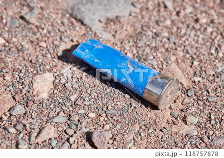 Plastic sleeve for a hunting-type cartridge for a smoothbore shotgun. Empty blue gun casing on a dirt road. Plastic sleeve for a hunting-type cartridge for a smoothbore shotgun. Empty blue gun casing on a dirt road. 118757878
