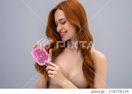 Ginger young woman holding a pink hairbrush in hands Ginger young woman holding a pink hairbrush in hands 118758134