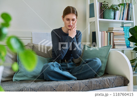 Young teenage female having toothache, sitting on couch at home Young teenage female having toothache, sitting on couch at home 118760415