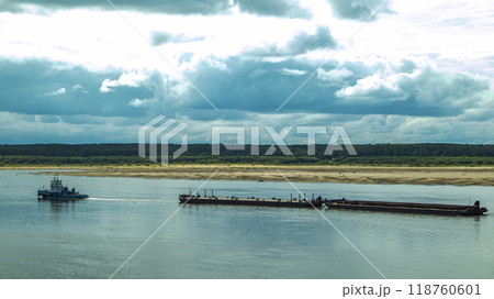 A large river vessel pulls two barges loaded with timber down the river A large river vessel pulls two barges loaded with timber down the river 118760601