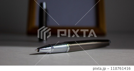 Pen on beautiful white fon on warm light. Wooden picture frame and cap in the background. Pen on beautiful white fon on warm light. Wooden picture frame and cap in the background. 118761416