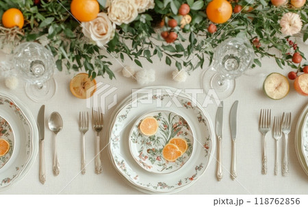 Romantic table setting with vintage plates, cutlery, and citrus fruits. Fresh flowers and greenery create an inviting atmosphere for a special dinner or celebration 118762856