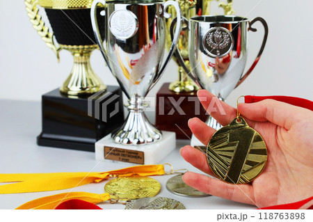 A person proudly holds a shining gold medal in front of trophies A person proudly holds a shining gold medal in front of trophies 118763898