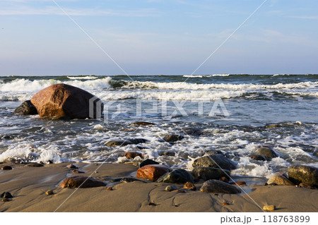 A large rock is resting on the sandy beach next to the ocean waves A large rock is resting on the sandy beach next to the ocean waves 118763899