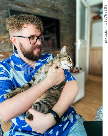 Warm moment between a millennial man and his cat, bond and affection shared in a cozy home environment. Portrait at home. Pet and friendship concept Warm moment between a millennial man and his cat, bond and affection shared in a cozy home environment. Portrait at home. Pet and friendship concept 118765105