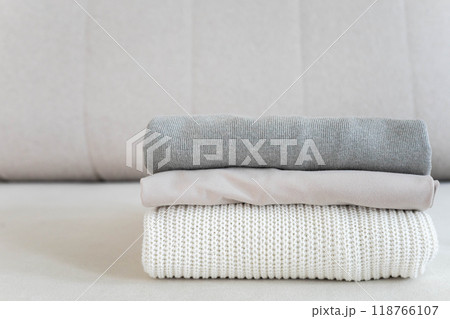A neat stack of clean knitwear in neutral colors lies on the sofa. 118766107