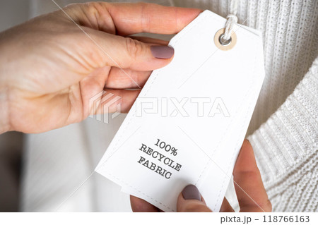 Female hands hold a label from white knitted clothing, on which it says 100 percent recycle fabric Female hands hold a label from white knitted clothing, on which it says 100 percent recycle fabric 118766163