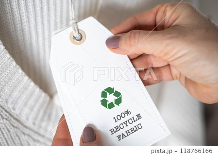Female hands hold a label from white knitted clothing, on which it says 100 percent recycle fabric 118766166