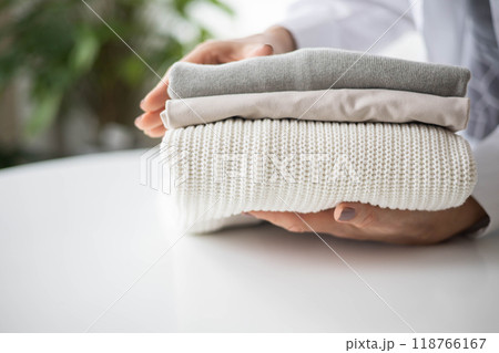 Women's hands hold a stack of neat, clean, cotton clothes in neutral shades. 118766167