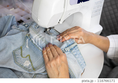 Clothes repair concept. Women's close-up hands sew up old faded blue jeans. 118766171