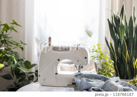 Workplace with a sewing machine. There are old blue jeans on the table. Workplace with a sewing machine. There are old blue jeans on the table. 118766187