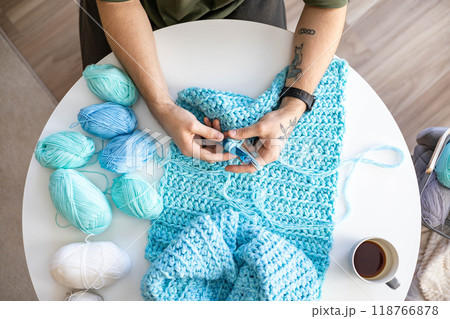 Male hands crochet handmade artwork use wool yarn and hook over table with coffee top view 118766878