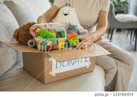 A woman puts toys in a cardboard box for charity. Donation concept. 118766954