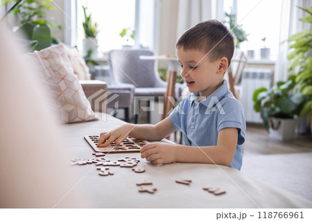 A Caucasian light-haired boy of five years old with blue eyes is putting together a puzzle 118766961