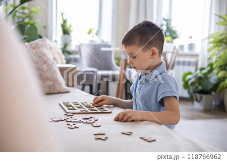 A Caucasian light-haired boy of five years old with blue eyes is putting together a puzzle 118766962