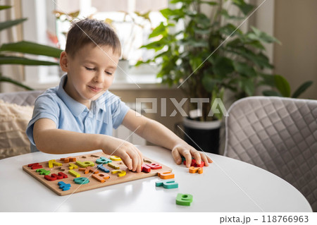A Caucasian light-haired boy of five years old with blue eyes is putting together a puzzle 118766963