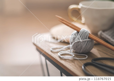 Cozy homely atmosphere. Female hobby knitting. Yarn in neutral colors in a white iron wire basket. Cozy homely atmosphere. Female hobby knitting. Yarn in neutral colors in a white iron wire basket. 118767015