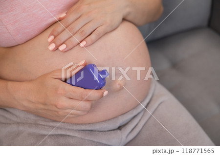 A pregnant woman smokes a vape while sitting on the couch. Close-up of the abdomen. A pregnant woman smokes a vape while sitting on the couch. Close-up of the abdomen. 118771565