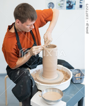 A potter works on a potter's wheel to smooth the surface of a vase. A potter works on a potter's wheel to smooth the surface of a vase. 118771573