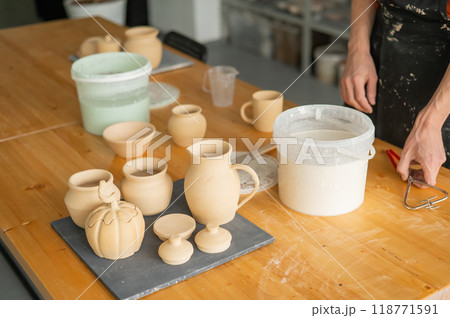 Close-up of a potter's hands glazing a ceramic mug. Close-up of a potter's hands glazing a ceramic mug. 118771591