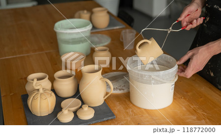 Close-up of a potter's hands glazing a ceramic mug. Close-up of a potter's hands glazing a ceramic mug. 118772000