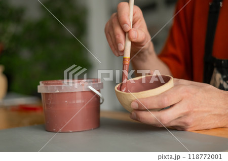 Close-up of a potter's hands with a brush painting ceramic dishes.  118772001