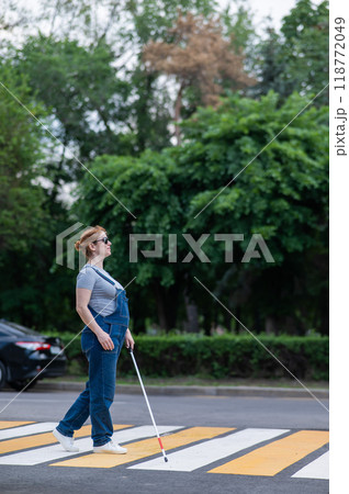 Blind pregnant woman crosses the road at a crosswalk with a cane.  118772049