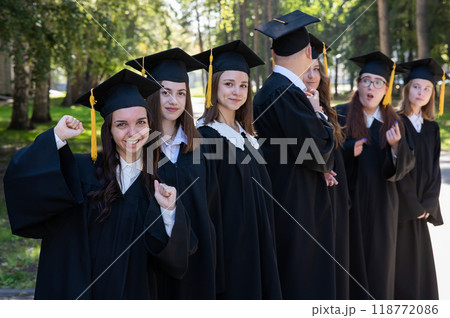 Row of happy young people in graduation gowns outdoors. Students in the park. Row of happy young people in graduation gowns outdoors. Students in the park. 118772086