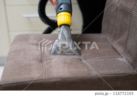 Woman cleaning a fabric chair with a professional washing vacuum cleaner.  118772105