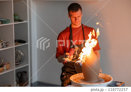 A potter burns a jug with a gas burner on a potter's wheel.  118772257