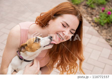 Dog jack russell terrier licks the owner in the face outdoors. Girl with braces on her teeth. Dog jack russell terrier licks the owner in the face outdoors. Girl with braces on her teeth. 118772337