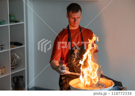 A potter burns a jug with a gas burner on a potter's wheel.  118772338