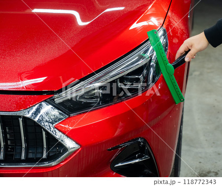 A man washes the headlights of a red car with a scraper. A man washes the headlights of a red car with a scraper. 118772343