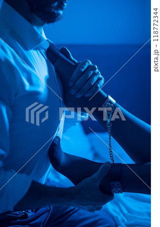A man holds a woman by the ankles. BDSM concept. Vertical photo.  118772344