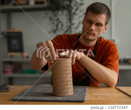 Potter sculpts a patterned cylinder from clay.  118772347