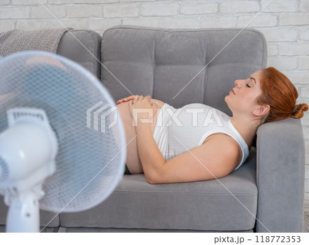 Pregnant woman suffers from heat and lies on the sofa near the electric fan.  118772353