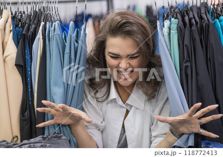 A fat woman in a plus size store peeks out from behind racks of clothes. A fat woman in a plus size store peeks out from behind racks of clothes. 118772413
