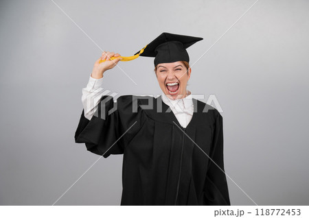 Smiling woman in graduation gown holding cap by tassel on white background. Smiling woman in graduation gown holding cap by tassel on white background. 118772453