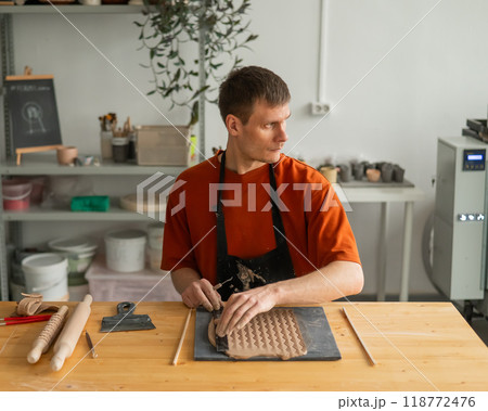 A potter cuts a piece of rolled clay with patterns.  A potter cuts a piece of rolled clay with patterns.  118772476