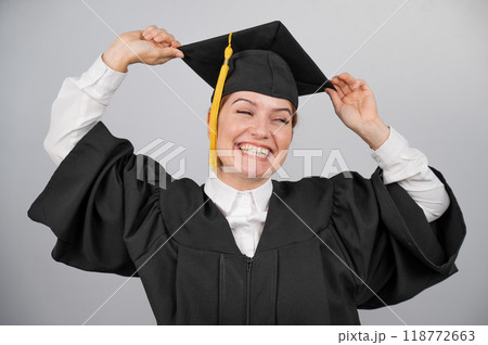 Smiling woman in graduation gown holding cap by tassel on white background. Smiling woman in graduation gown holding cap by tassel on white background. 118772663