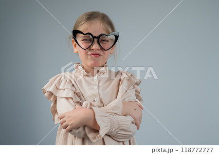 Portrait of a cute little girl grimacing wearing heart-shaped glasses on a white background.  118772777