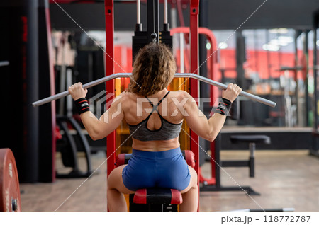 Rear view of a Caucasian forty-year-old woman doing lat pull-downs in the gym.  118772787