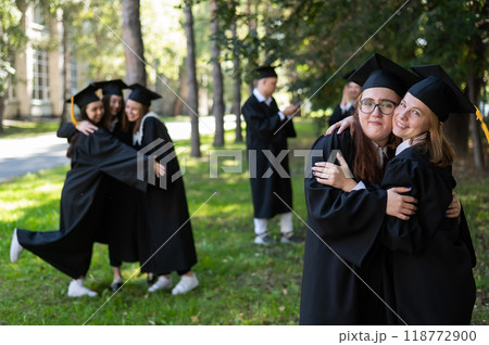 A group of graduates in robes congratulate each other on their graduation outdoors. 118772900