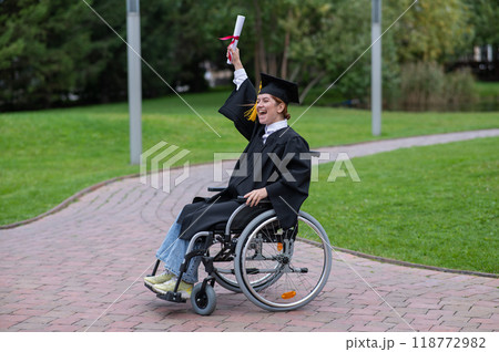 Caucasian woman in a wheelchair in a graduate costume rejoices at receiving a diploma. Caucasian woman in a wheelchair in a graduate costume rejoices at receiving a diploma. 118772982