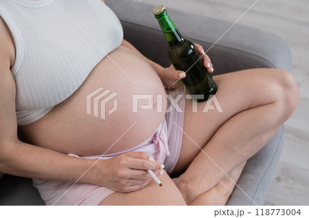 Faceless pregnant woman drinks beer while sitting on the sofa.  118773004
