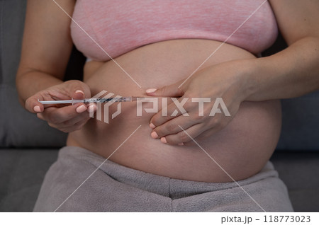 A pregnant woman puts an injection of insulin while sitting on the couch. Close up of the belly. 118773023